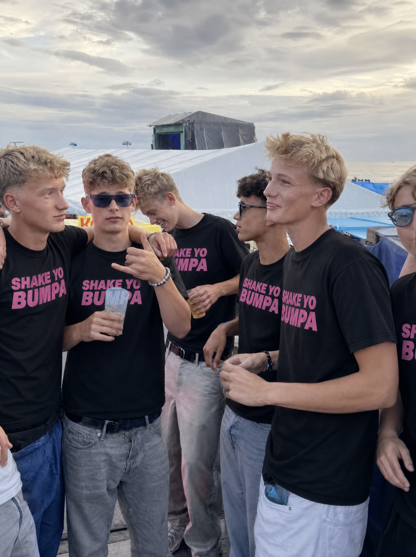 Groep vrienden in Shake Ur Bumpa shirts bij zonsondergang op een festival